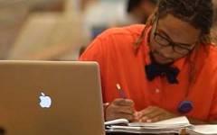 Student writing at desk with laptop.